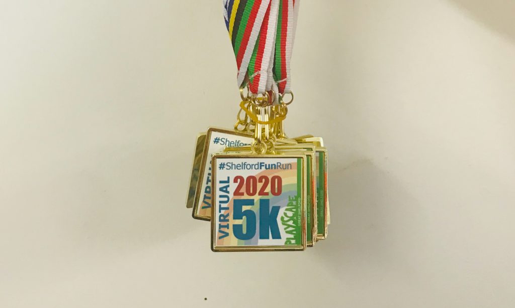 Close up photo of a number of Shelford Fun Run 2020 medals being held up against a white wall