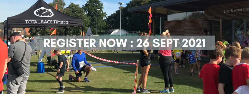 Photo at the Shelford fun run start line, with chip timing tent on the left and sports pavilion on the right. People chatting and stretching. Text: Register Now! 26 Sept 2021